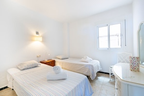 Habitación de hotel con dos camas, una mesita de noche, una silla, un espejo y una ventana.
