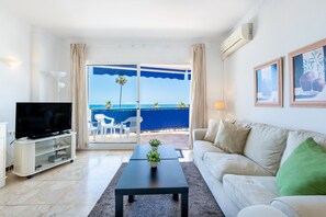 A living room with a television, a sofa, a coffee table, and a view of the ocean. - Maritimo Rey | Beach Front Apartment in Fuengirola (Fuengirola)