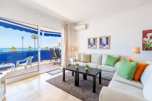 A living room with a sofa, two side tables, a coffee table, and a view of the sea through large glass doors. - Maritimo Rey | Beach Front Apartment in Fuengirola (Fuengirola)