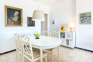 A dining area with a white table and chairs, a hanging lamp, and wall art. - Maritimo Rey Fuengirola | Charming Beachfront Apartment with Sea View Balcony (Fuengirola)
