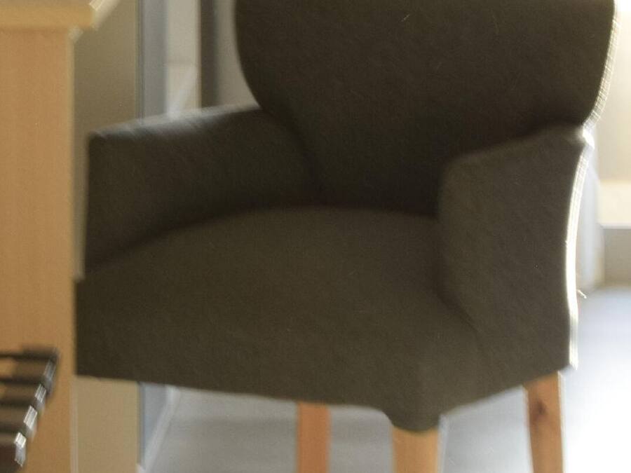 Een moderne stoel met donkere bekleding en houten poten, geplaatst naast een houten bureau met een afstandsbediening erop.