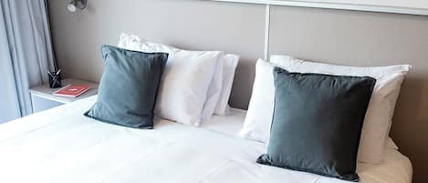 A neatly made bed with white and dark grey pillows, a grey throw blanket, and a framed historical map on the wall.