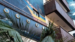 Une façade d’immeuble ornée d’une fresque murale, avec des fenêtres rondes et des palmiers au premier plan.