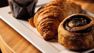Un plato con un croissant, un rollo de canela y un muffin sobre una mesa de madera.