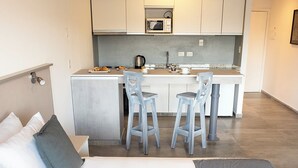 Une chambre d’hôtel moderne équipée d’un lit, d’une petite kitchenette et de deux tabourets de bar.