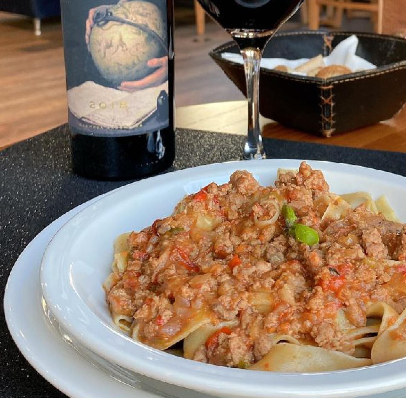 A plate of pasta with a meat sauce, a wine bottle, and a glass of red wine on a table.