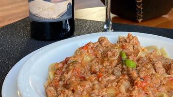 A plate of pasta with a meat sauce, a wine bottle, and a glass of red wine on a table.