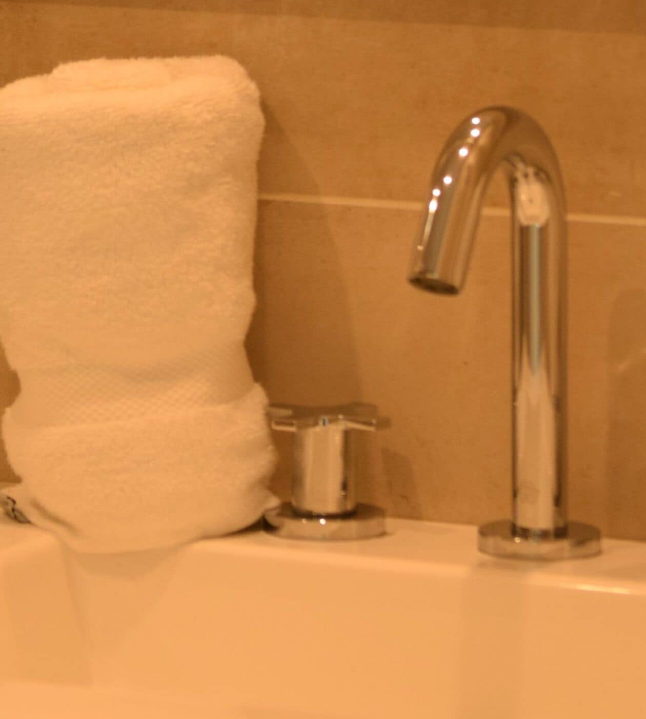 Una toalla blanca colgada en un perchero de metal en un baño con un grifo cromado.