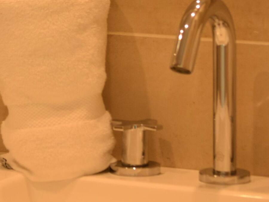 Una toalla blanca colgada en un perchero de metal en un baño con un grifo cromado.
