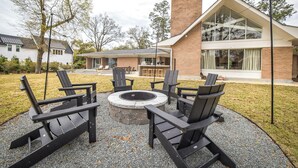 Una zona relax esterna moderna con poltrone Adirondack e un braciere circolare, immersa in un patio con ghiaia.