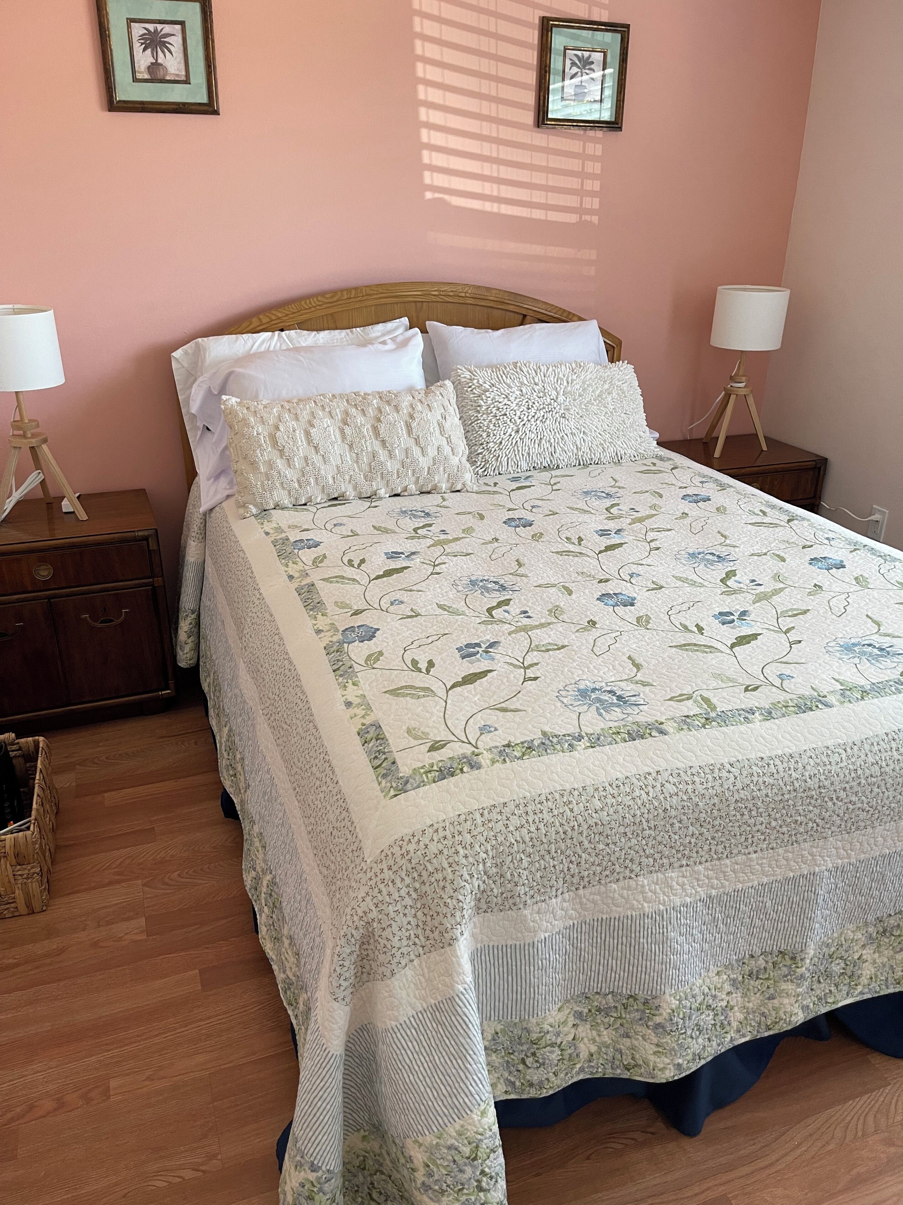 A neatly made bed with a floral quilt, two bedside tables with lamps, and a wooden floor.