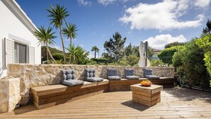 Una terraza al aire libre con un muro de piedra, asientos de madera y una mesa pequeña con fruta.
