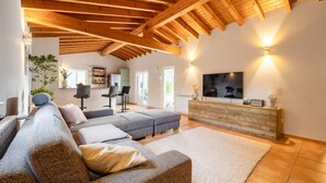 Un salón espacioso con techo de madera, un sofá grande, un televisor y un mueble de madera.