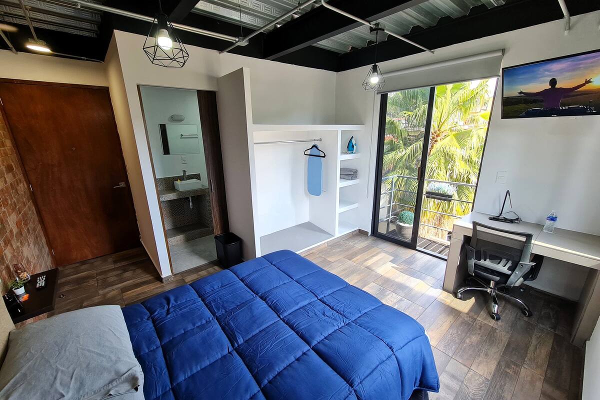 A modern bedroom with a large bed, a desk, and a balcony with a view.