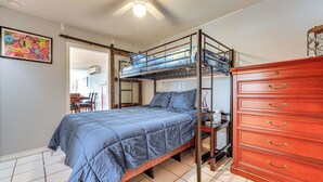 Un letto a castello con materasso blu, un comò in legno con cassetti e una ventola a soffitto.