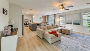 Ein geräumiges Wohnzimmer mit einem großen Ecksofa, einer Küche im Hintergrund und einem Deckenventilator.