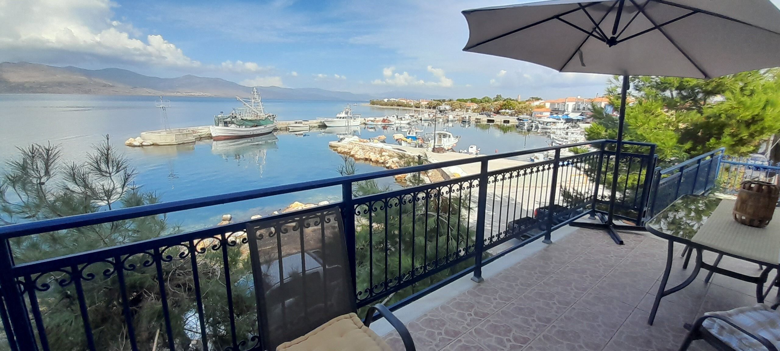 Ein Balkon mit Blick auf eine Marina, ein Tisch mit Stühlen und ein Sonnenschirm.