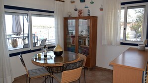 Een eetgedeelte met een ronde tafel, stoelen, een boekenkast en uitzicht door het raam.