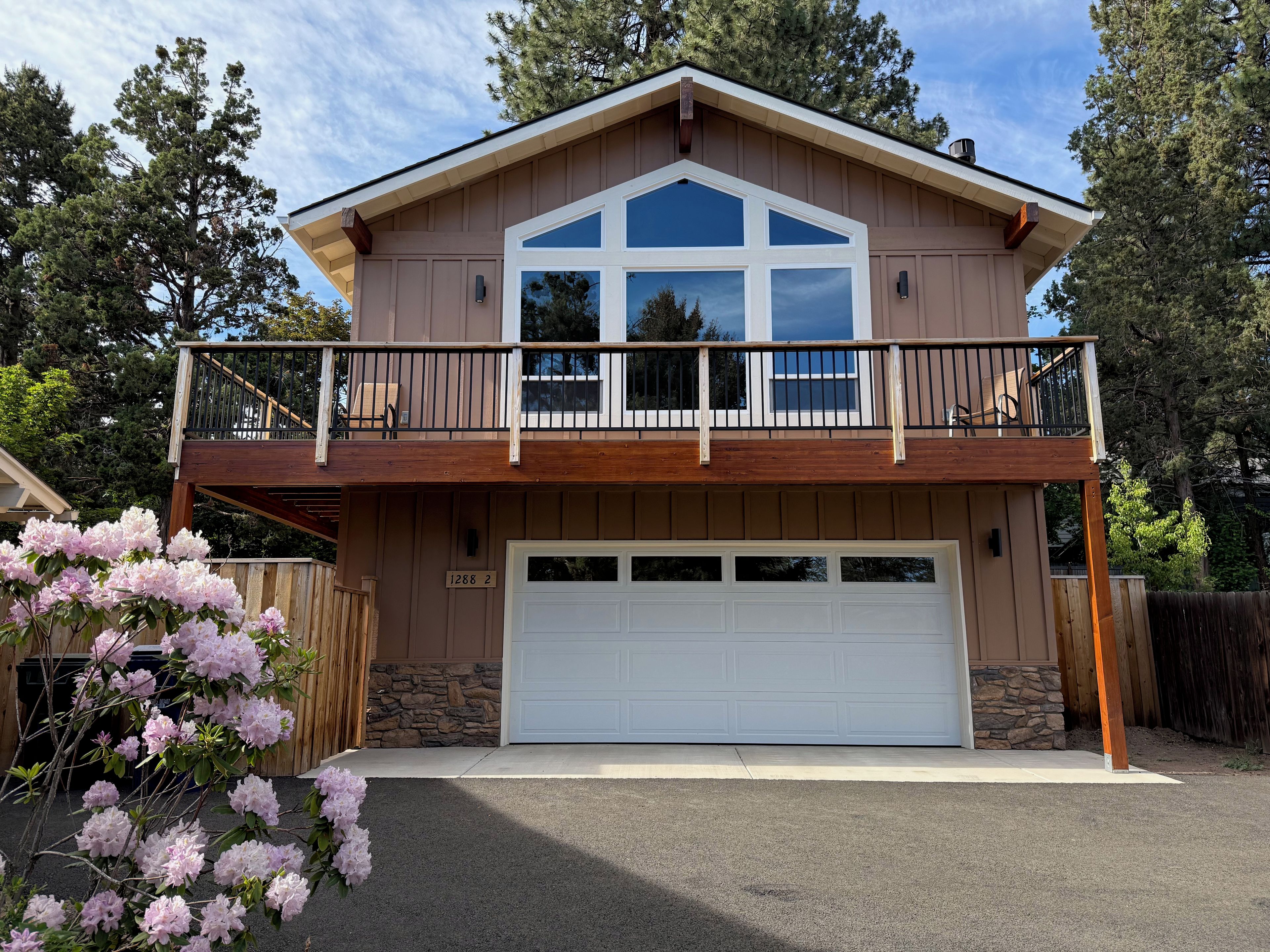 Une maison à deux étages avec un balcon, un garage et des fondations en pierre.