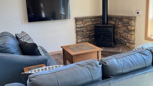 A living room with a stone fireplace, a television mounted on the wall, and a sofa with cushions. - HideAway Chalet, perfect destination for peace, relaxation retreat,  adventure (Bend)