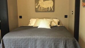 Una cama con una colcha gris acolchada, un almohadón estampado con rayas y un cuadro de un elefante colgado en la pared.