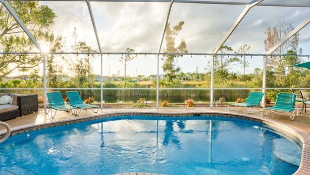 A swimming pool with a covered area, green lounge chairs, and a view of the surrounding landscape.