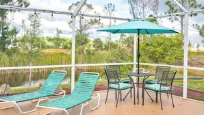 A covered outdoor area with a table and chairs, a green umbrella, and lounge chairs.