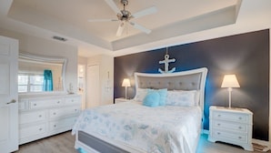 A bedroom with a bed, nightstands, a dresser, a ceiling fan, and a wall with an anchor decoration.