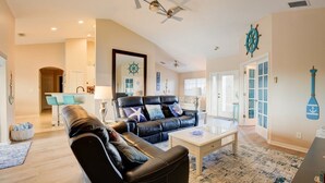 A spacious living room with a black leather sofa, a coffee table, and a ceiling fan.