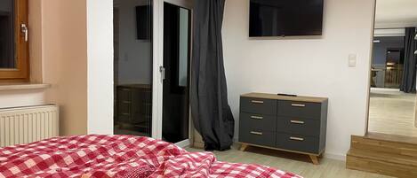 Un dormitorio con cama, cómoda, televisor y puerta corredera.