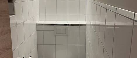 Ein kleines Badezimmer mit weißen Fliesen, einer Toilette, einem Waschbecken und einem Handtuchhalter.