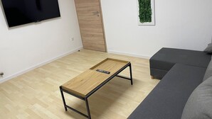 En moderne stue med et træ sofabord, en grå sofa, et fladskærms-tv monteret på væggen og en trædør.