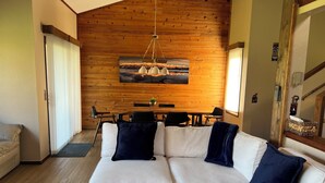 Een moderne woonkamer met een hoekbank, een eettafel en een houten wand met een schilderij.
