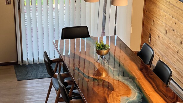 Een eettafel met een glazen blad en houten frame, omringd door zwarte stoelen.