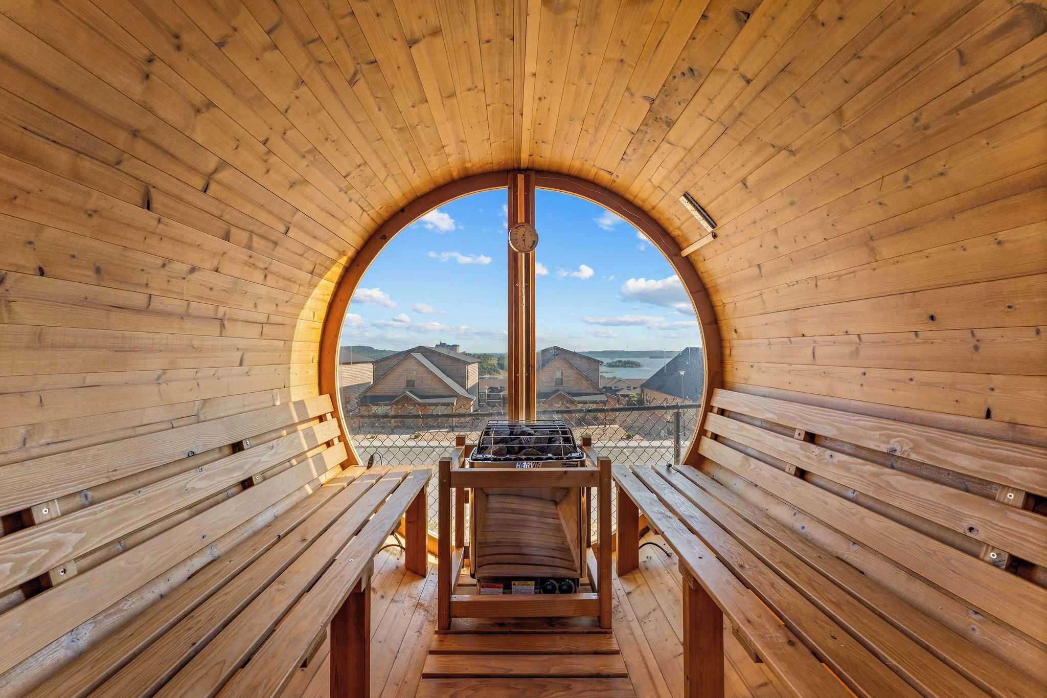 A wooden interior with benches and a central grill area, featuring a clear view of buildings and water outside.