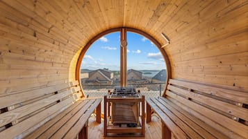 A wooden interior with benches and a central grill area, featuring a clear view of buildings and water outside.
