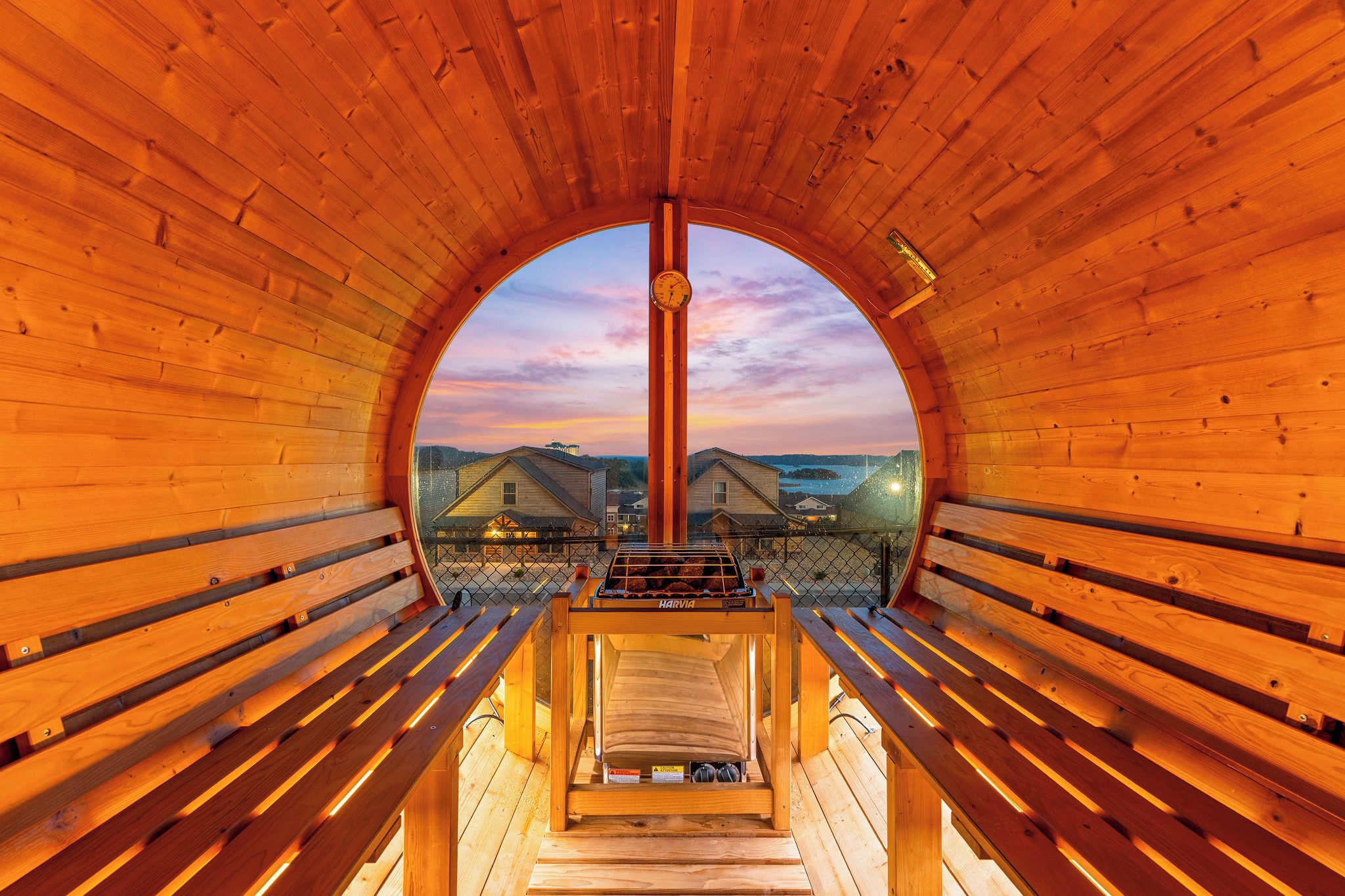 A circular wooden structure with benches and a central pole, offering a view of houses and a body of water.