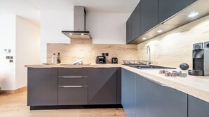 A modern kitchen with dark cabinets, a wooden countertop, and a built-in stove. - Opale - Cozy apartment with terrace in Megève (Megeve)