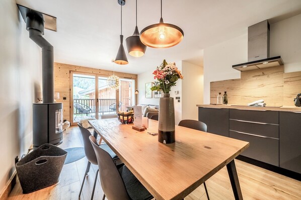 A modern kitchen with a wooden dining table, pendant lights, and a built-in stove. - Opale - Cozy apartment with terrace in Megève (Megeve)