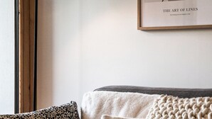 A cozy room with a framed artwork titled "THE ART OF LINES" on the wall, a modern floor lamp, and a sofa with patterned cushions. - Opale - Cozy apartment with terrace in Megève (Megeve)