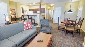 A living room with a sofa, a coffee table, and a dining area with chairs and a table. There is a kitchen in the background with cabinets and a microwave. - WorldMark Bison Ranch - 1 Bedroom (Overgarrd)