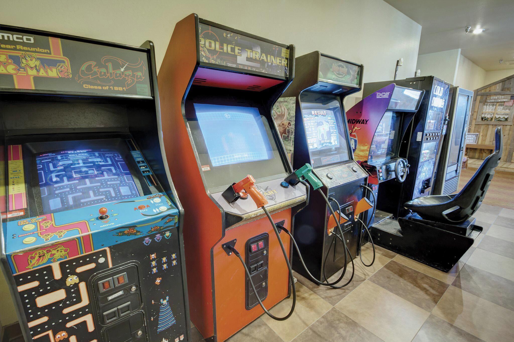 A row of arcade machines, including a police training game and a maze game, in a public space.