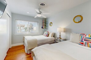 A bedroom with two beds, a ceiling fan, a window with blinds, a bedside table with a lamp, and a wall-mounted mirror. - Dog-friendly house with ocean view, balcony, gas grill, patio, central AC & W/D (Port Aransas)