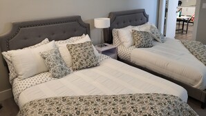 A hotel room with two beds, each with a headboard, a bedside table with a lamp, and a painting on the wall.