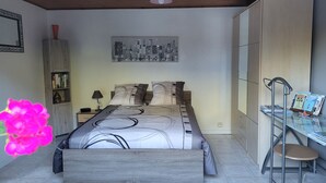 A bedroom with a bed, a desk, a chair, a bookshelf, and a cityscape painting on the wall. - Appartement au Calme (Bonnevaux)