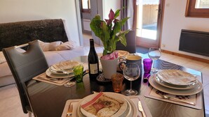 A dining table set with plates, glasses, cutlery, a bottle of wine, and a potted plant. - Appartement au Calme (Bonnevaux)