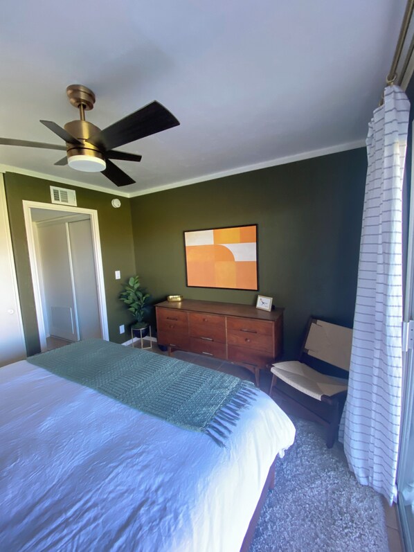 A bedroom with a bed, a ceiling fan, a dresser, a chair, and a painting on the wall.