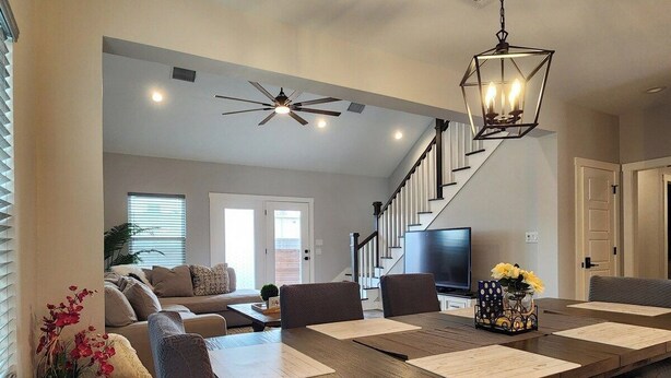 A spacious living room with a large wooden dining table, comfortable seating, a staircase, and a television. - Modern Retreat in Sherman TX (Sherman)