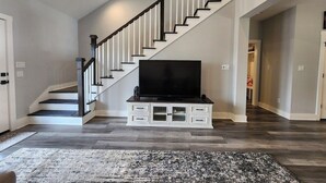 A staircase with a black railing, a flat-screen TV on a white cabinet, and a patterned rug on the floor. - Modern Retreat in Sherman TX (Sherman)