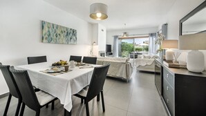 Ein moderner Essbereich mit einem weißen Tisch und Stühlen, einem Bild an der Wand und Blick ins Freie durch große Fenster.